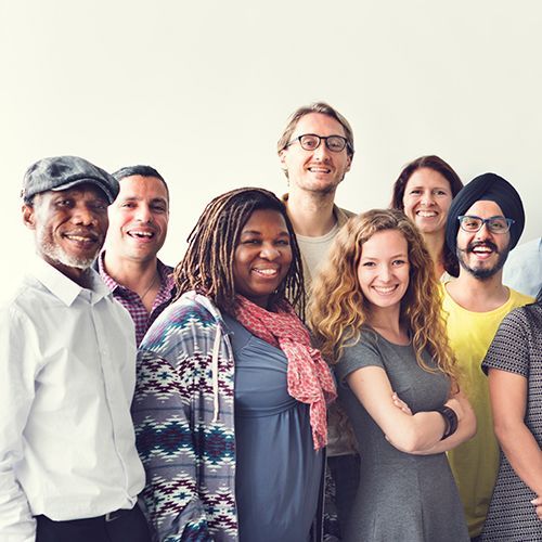 Ein Gruppenfoto von mehreren Erwachsenen, die allesamt unterschieldicher Herkunft sind. Sie l&auml;cheln vergn&uuml;gt in die Kamera.