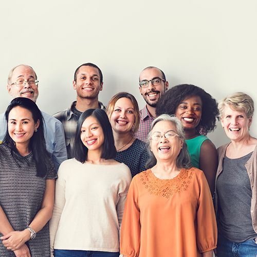 Ein Gruppenfoto von mehreren Erwachsenen, die allesamt unterschieldicher Herkunft sind. Sie l&auml;cheln vergn&uuml;gt in die Kamera.