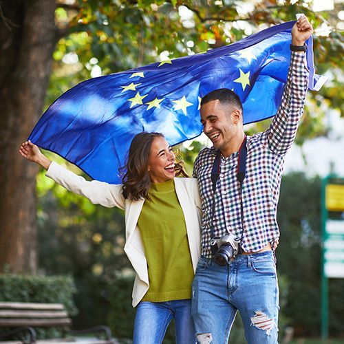 Ein junges Paar h&auml;lt erfreut eine Europa-Flagge &uuml;ber ihren K&ouml;pfen.