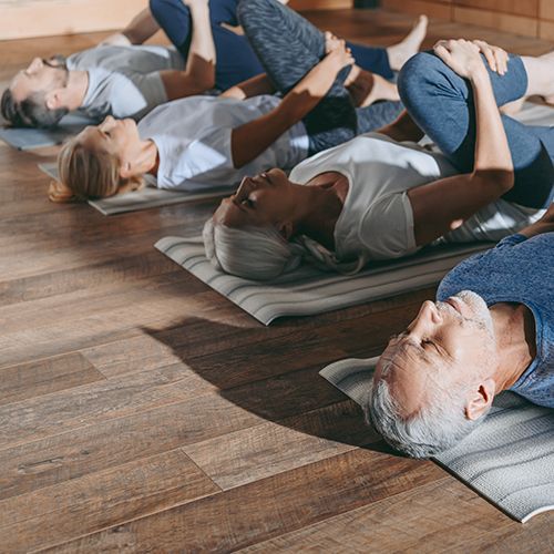 Eine Gruppe &auml;lterer Menschen praktiziert Yoga-&Uuml;bungen im Liegen.
