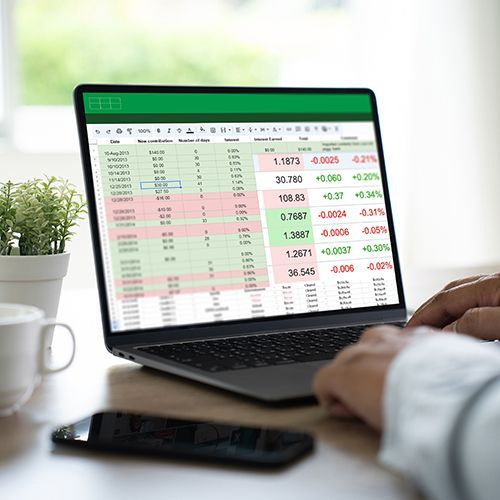 Man sieht einen Laptop, auf dem eine Excel-Tabelle mit verschiedenen Zahlen und farbig markierten Zeilen zu sehen ist. Ein Man sitzt davor, man sieht seine Hand auf der Tatstatur.