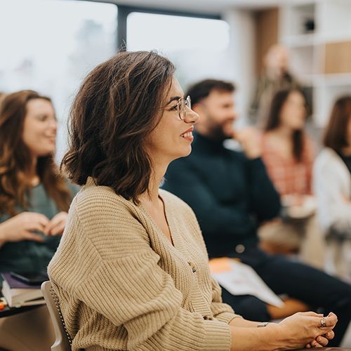 Lächelnde Frau, die mit Teilnehmende an einem Workshop in einer modernen Büroumgebung teilnimmt.