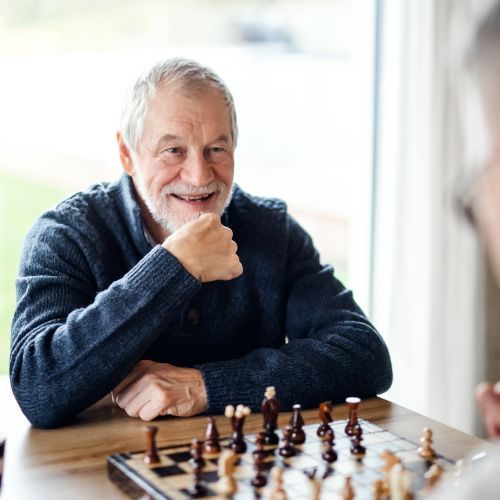 Ein älterer Mann spielt Schach und hält sich eine Hand ans Kinn.