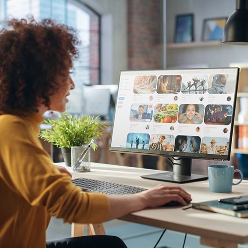 Eine Frau sitzt vor einem großen Monitor und schaut sich Bilder an. Dahinter ist ein offenes Regal.