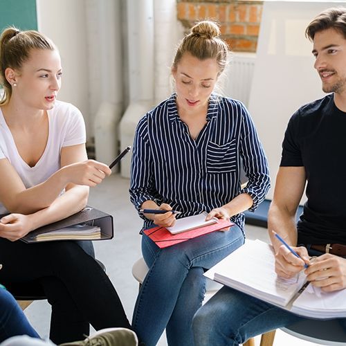 Drei junge Personen sitzen in einem Stuhlkreis und diskutieren.
