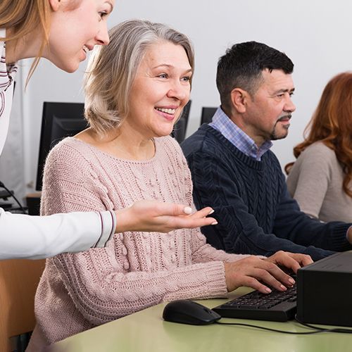 Drei Personen sitzen vor Computern und eine junge Frau erklärt einer Teilnehmerin etwas.