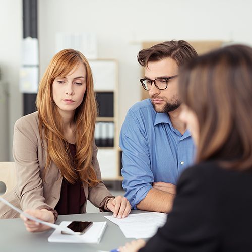 Drei Personen schauen sich Unterlagen in einem hellen Büroraum an. Eine Frau hält ein Blatt für alle in die Höhe.