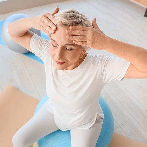 Eine Frau sitzt auf einem Gymnastikball und hält sich massierend die Hände auf die Stirn.
