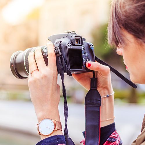 Eine junge Frau bedient eine Spiegelreflexkamera, um etwas zu fotografieren.