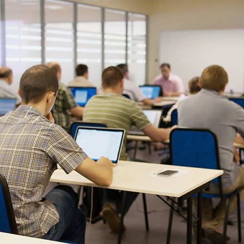 In einem Coputerraum sitzen M&auml;nner mit dem R&uuml;cken zur Kamera vor Laptops.