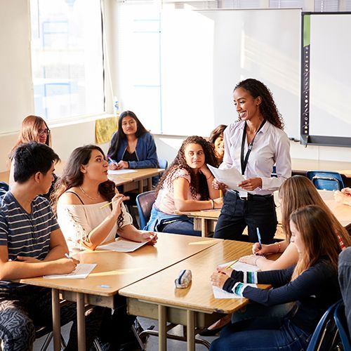 Eine weibliche Dozentin steht vor einem Tisch in einem Kursraum und erkl&auml;rt den Kursteilnehmenden etwas