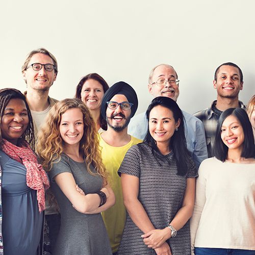 Ein Gruppenfoto von mehreren Erwachsenen, die allesamt unterschieldicher Herkunft sind. Sie l&auml;cheln vergn&uuml;gt in die Kamera.