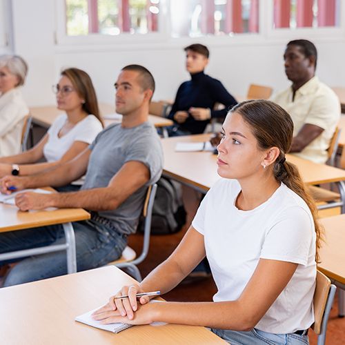 Mehrere sowohl j&uuml;ngere als auch &auml;ltere Seminarteilnehmer sind an ihren Tischen und h&ouml;ren aufmerksam der Lehrkraft zu.