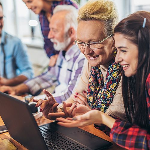 Vier Studierende und eine Lehrkraft in einem Raum. Die Studierenden sitzen vor Laptops. Die Stimmung ist freudig.