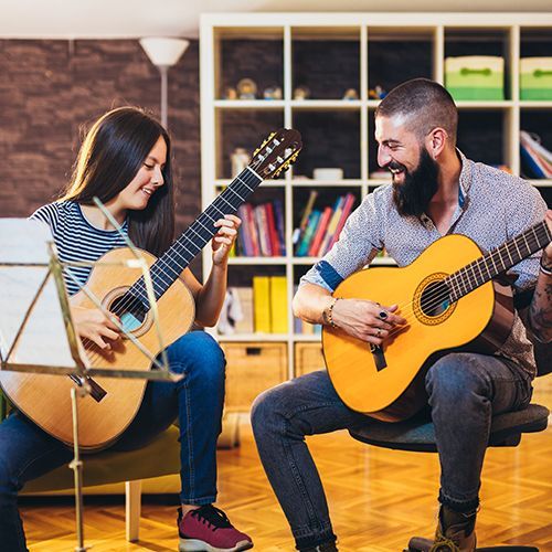 Ein Gitarrenlehrer bringt einer Gitarrensch&uuml;lerin Gitarre  spielen bei.