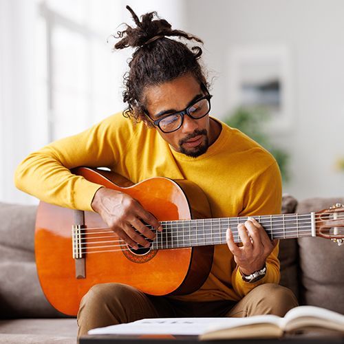 Junger, fr&ouml;hlicher Afroamerikaner spielt zu Hause auf dem Sofa im Wohnzimmer Akustikgitarre.
von JenkoAtaman