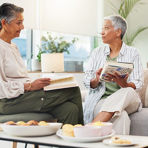 Vier Menschen (&Uuml;50) in einem Raum die sich unterhalten. Zwei halten ein Buch in der Hand. Alle sind aufmerksam. Neben ihnen steht ein kleiner Tisch mit Obst.
