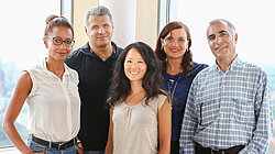 Zwei Männer und drei Frauen unterschiedlicher Herkunft stehen als Gruppe zusammen und lächeln gemeinsam in die Kamera.