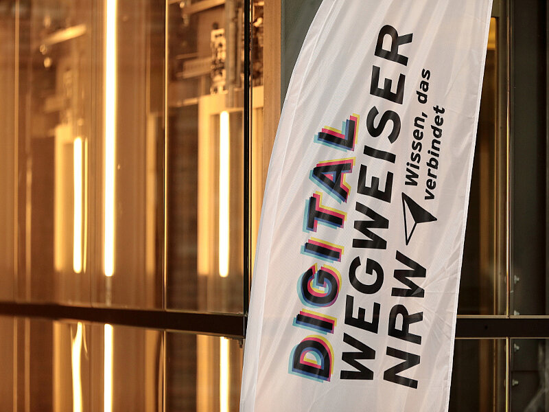 Öffnet die Seite 'Digitalwegweiser NRW: Austausch und Praxis' Aufsteller mit Aufschrift Digitalwegweiser NRW