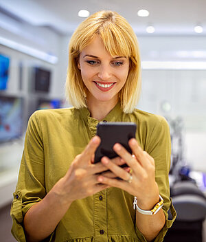 Eine Frau in gelber Bluse schaut mit einem Lachena ihr Smartphone