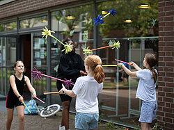 Vier Mädchen üben das Jonglieren mit Flower Sticks. Sie halten je einen Stab in einer Hand und versuchen dabei einen dritten Stab in die Luft zu werfen.