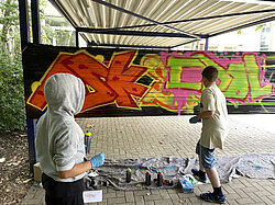Zwei Jungen nutzen ihre Kreativität, indem sie ein Graffiti auf eine schwarze Folie sprühen.
