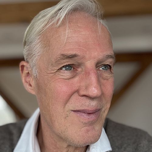 Ein Gesicht eines Mannes von der Seite mit grau/weißen Haaren.