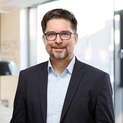 Dozent mit dunklen Haaren und Brille bekleidet mit Hemd und Sakko