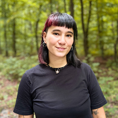 Dozentin steht im Wald und lächelt in die Kamera